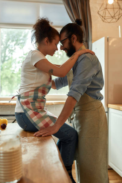 istock Young man looking at his girlfriend, hugging while standing in the kitchen. Couple embracing while cooking together indoors. Hobby, lifestyle 1266848833