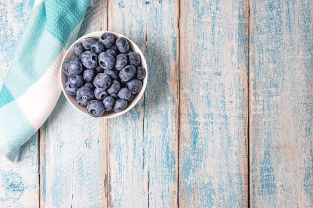 Top down overhead shot of a white bowl filled with fresh juicy blueberries on a rustic weathered worn light blue wood table surface