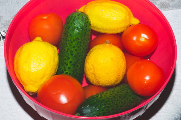 Tomatoes and cucumbers in a red bowl. lemons in water. fresh vegetables