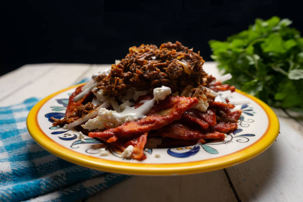 Mexican red chilaquiles with chilorio and cheese on white background