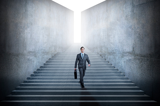A businessman carrying a briefcase walks down a long set of stairs bounded by large concrete walls.\