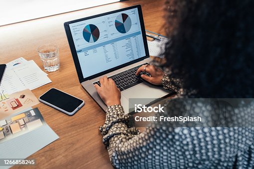 istock Anonymous Businesswoman Analyzing Statistical Business Reports on her Laptop PC at the Office, a Close Up 1266858245