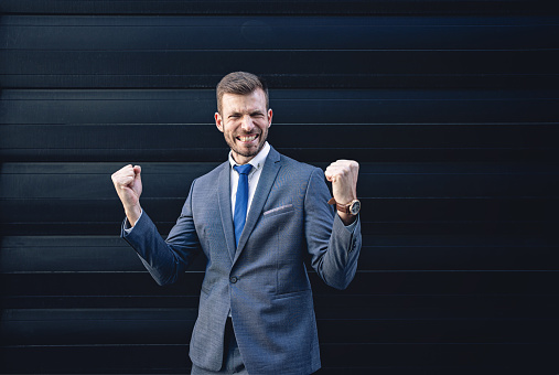 Confident businessman standing in formalwear with arms raised celebrating success.