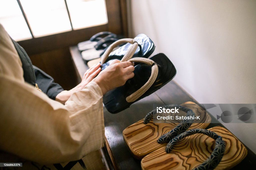 Japanese woman picking up ‘Zori’ sandal at the entrance of traditional Japanese ‘Ryokan’ hotel Geta Sandal Stock Photo
