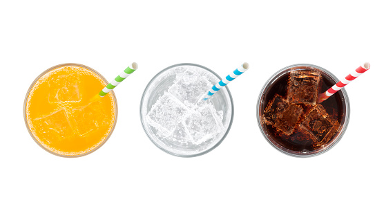 Top view of glasses of orange soda, lemon lime soda and cola drinks with ice and straws isolated on white