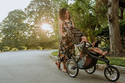 Black mom pushing a baby stroller outdoors during summer