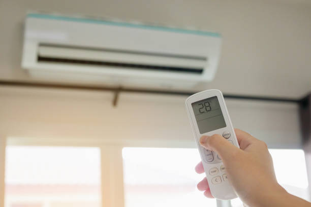 istock Hand with remote control directed on air conditioner inside the room 1266868375