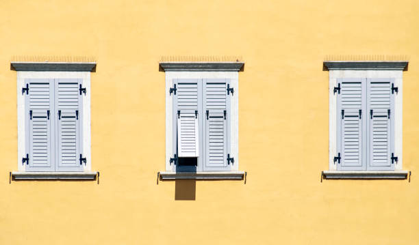istock Three Italian windows on the yellow wall facade with closed light grey color classic shutters 1266871712