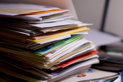Large stack of financial bills, letters, cards, and advertisements on a home office desk, waiting to be opened.