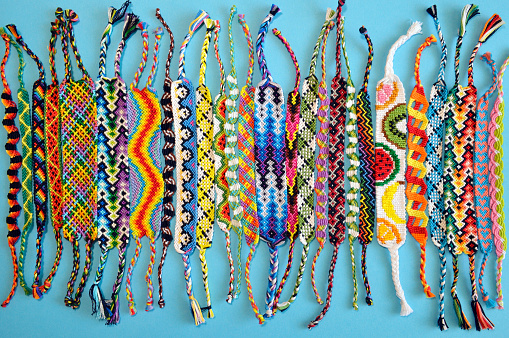 Multi-colored woven friendship bracelets handmade of embroidery bright thread with knots isolated on blue background