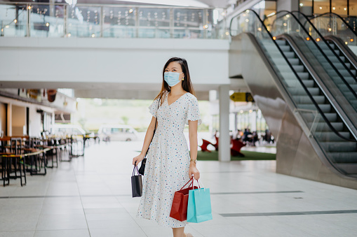 Happy young Asian woman wearing face mask and enjoying shopping