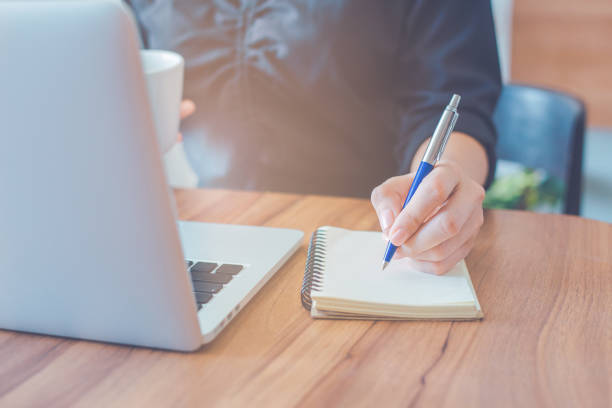 istock Woman is writing on a notebook with a pen and using a laptop to work in the office. 1266891223