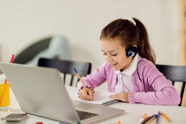 istock Happy schoolgirl writing while e-learning over laptop at home. 1266903181