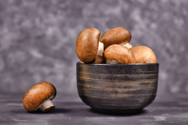 istock Raw brown button mushrooms in bowl on dark background 1266903605