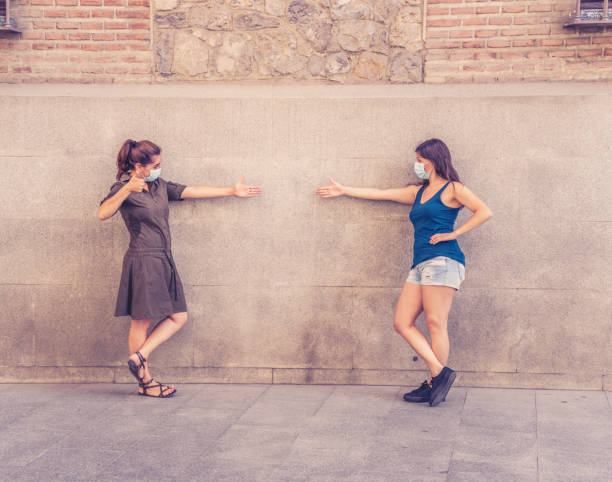 istock Two woman wearing protective face masks standing 2 m from each other keeping social distancing avoiding the spread of coronavirus. Conceptual image of COVID-19 disease protection and New Normal. 1266904621