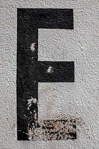 capital letter E painted on a house wall with chipped paint