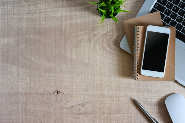 istock Office desk wood table with smartphone with empty screen, laptop, and supplies. Top view with copy space, flat lay. 1266909742