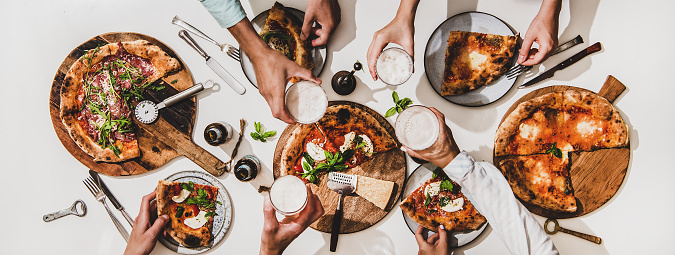 Pizza party for friends or family. Flat-lay of various pizzas, drinks and people celebrating with beer over plain white table background, top view. Fast food, comfort food, Italian cuisine concept