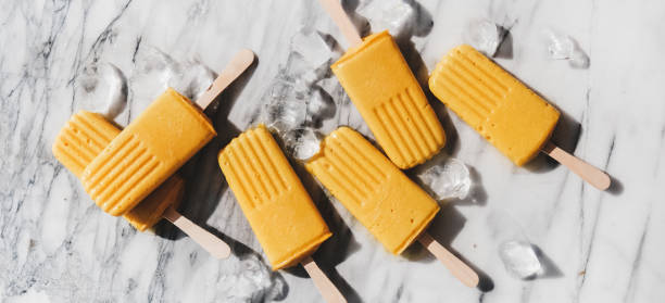 istock Homemade mango smoothie vegan popsicles over marble background, wide composition 1266913546