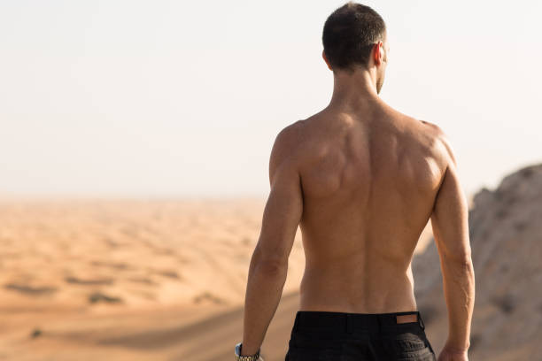 homem forte sem camisa em pé acima olhando a vista das dunas do deserto. fitness ao ar livre e desafio. - men sensuality photography high angle view - fotografias e filmes do acervo