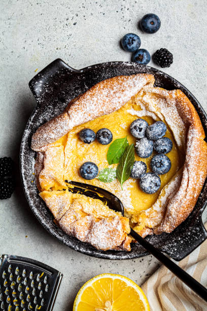 Dutch baby pancake with berries and lemon in cast iron frying pan, top view. Dutch baby pancake with berries and icing sugar in a pan. pancake photos stock pictures, royalty-free photos & images