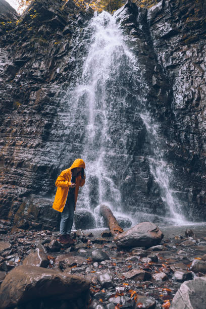 istock woman in yellow raincoat at autumn waterfall 1266925762
