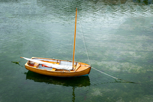 An image of a wooden sailboat in quaint harbour of the picturesque fishing village of Mousehole in Cornwall, UK which is a popular tourist destination on a beautiful summer day.