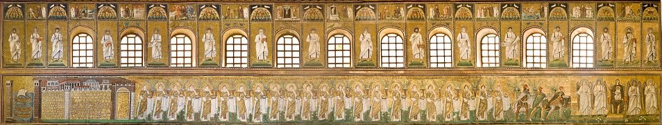 Panorama of the left lateral wall mosaics in the Basilica of Sant'Apollinare Nuovo, Ravenna, Emilia-Romagna, Italy. It shows the procession of 22 virgins, led by the Three Magi, moving from the city of Classe towards the group of the Madonna and Child surrounded by four angels. 32 depictions of apostles and prophets can be seen between the windows. Above it are alternating representations of the miracles and the Passion of Christ in rectangular fields. The Basilica - erected by the Ostrogothic king Theodoric the Great as his palace chapel during the first quarter of the 6th century - is one of the eight structures in Ravenna registered as UNESCO World Heritage Sites.