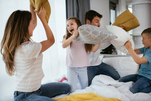 familia feliz tener una foto de acción de lucha de almohadas - bed couple pillow fight men fotografías e imágenes de stock