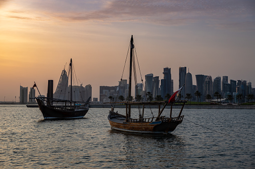Doha skyline from Museum of Islamic Art Park sunset shot showing dhows with Qatar flag in the Arabic gulf  in foreground and clouds in the sky in background