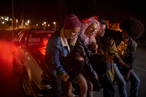 Multiethnic group of people having fun leaning on car at night Multiethnic hipster group of people having fun leaning on car at night on parking lot parking lot photos stock pictures, royalty-free photos & images