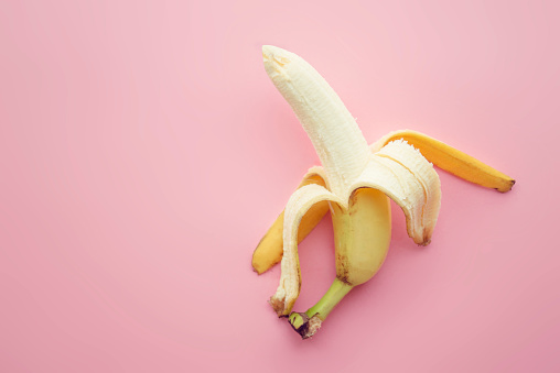 Half peeled banana on a pink background