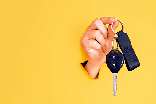 Female car salesperson holding a car key. Close up car keys on yellow background