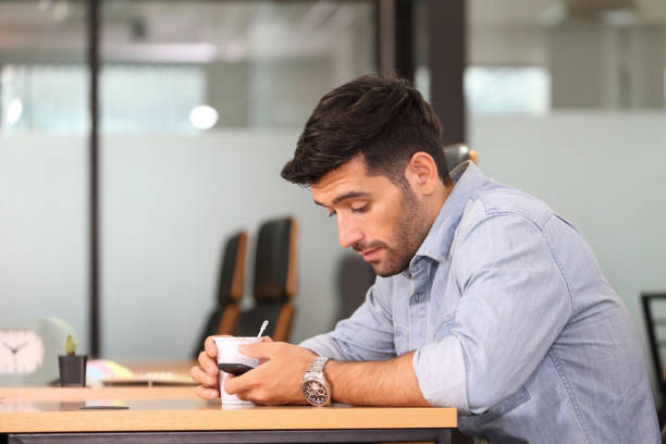 istock Caucasian businessman having coffee break while browsing online using cellphone in the office 1266944473