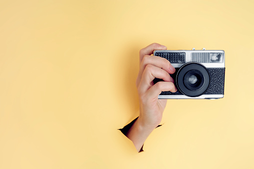 A female hand holding a vintage film camera on yellow background
