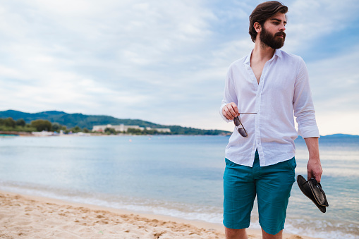 Handsome casually dressed bearded man walking at the beach on a sunny summer day during his vacation in Greece