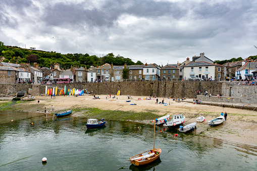 A landscape image of the quaint harbour and seafront of the picturesque fishing village of Mousehole in Cornwall, UK which is a popular tourist destination on a beautiful summer day.