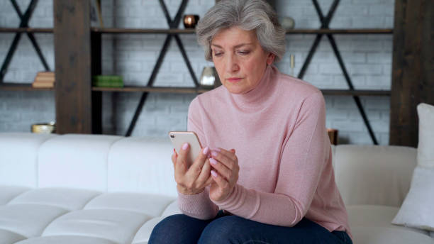 istock Cheerful mature woman sitting on the sofa and using a mobile phone 1266949768
