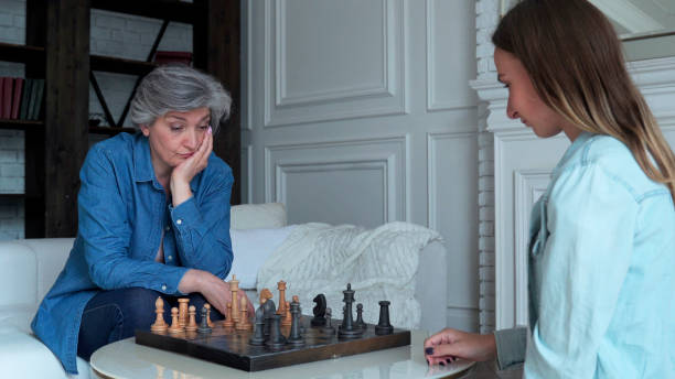 la mère et la fille jouent aux échecs s’asseyant sur le sofa dans le salon - chess board room business strategy photos et images de collection