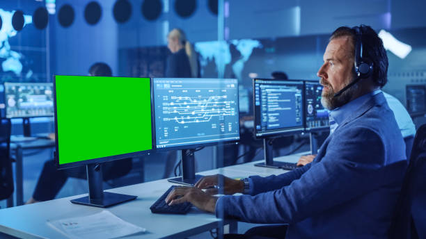 istock Confident Male Data Scientist Works on Computer with Green Screen Mock Up Template in Big Infrastructure Control and Monitoring Room. Senior Engineer in Call Center Office Room with Colleagues. 1266953116