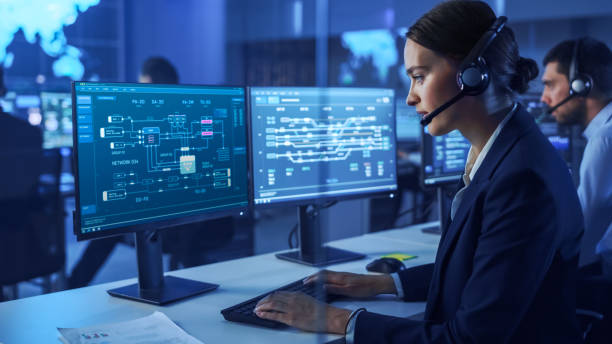 istock Confident Female Data Scientist Works on Personal Computer Wearing a Headset in Big Infrastructure Control and Monitoring Room. Woman Engineer Works with Network Logics in Office Room with Colleagues. 1266953117