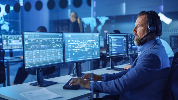 istock Confident Male Data Scientist Works on Personal Computer Wearing a Headset in Big Infrastructure Control and Monitoring Room. Senior Engineer in a Call Center Office Room with Colleagues. 1266953137