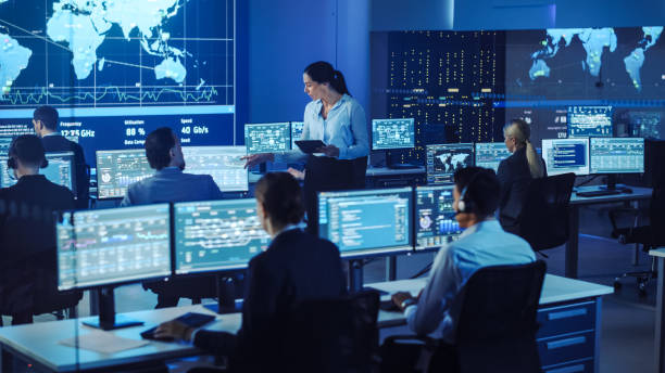 istock Female Project Leader with Tablet Computer Walks to a Male Data Science Engineer and Checks Up on His Work Progress. Telecommunications Control Monitoring Room with a Global Map on Big Screen. 1266953144