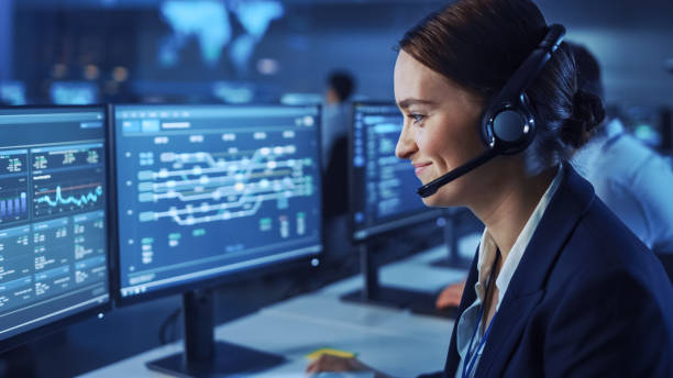istock Beautiful Female Data Scientist Works on Personal Computer Wearing a Headset in Big Infrastructure Control and Monitoring Room. Woman Engineer in a Call Center Office Room with Colleagues. 1266953148