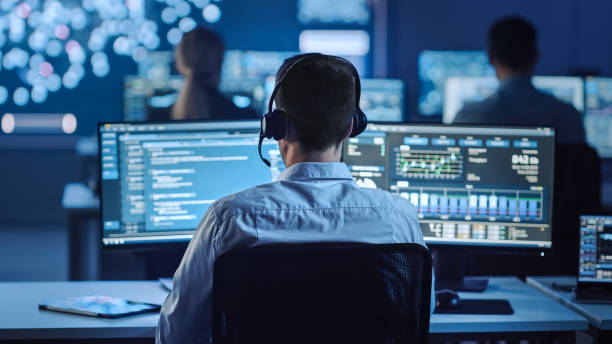 istock Confident Male Data Scientist Works on Personal Computer in Big Infrastructure Control and Monitoring Room with Neural Network. Young Engineer in an Office Room with Colleagues. 1266953291