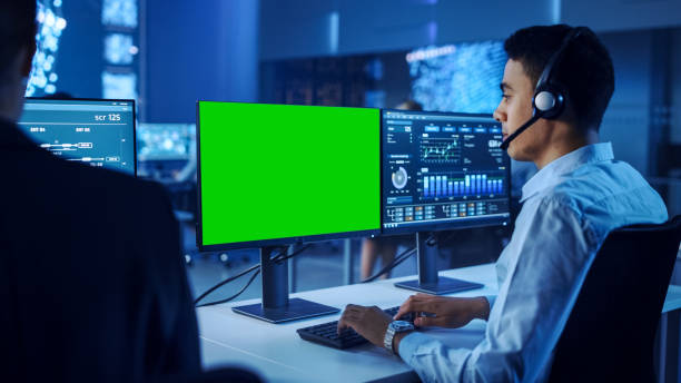 istock Confident Male Data Scientist Works on Personal Computer with Green Screen Template Wearing a Headset in Big Control and Monitoring Room. Young Engineer in a Call Center Office Room with Colleagues. 1266953313