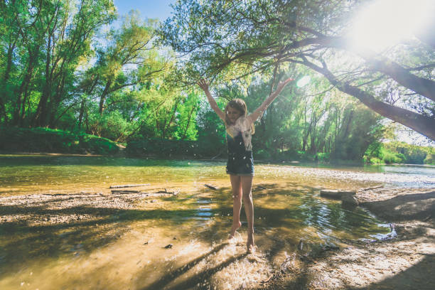 active girl having fun in shallow river in golden hour time in romantic green park
