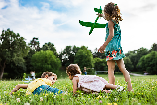 Boy and two girls are catching a plane in the meadow field. Leisure games.