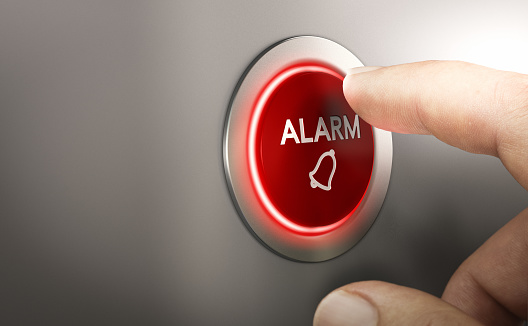 Finger pressing a red alarm button. Warning concept. Composite image between a hand photography and a 3D background.