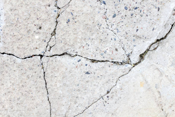 istock Concrete surface with cracks without painting with clearly visible pebbles of different sizes as a background 1266969532